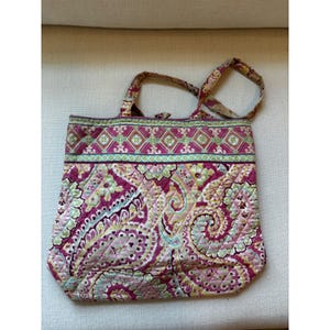 Puede incluir: Un bolso tote acolchado con un estampado de cachemira en tonos rosa, morado y amarillo. El bolso tiene dos asas y forma rectangular. La parte superior del bolso presenta un diseño geométrico en verde y rosa.