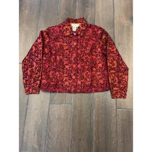 May include: A long-sleeve button-down jacket in a deep red and orange hue, featuring a prominent dark red velvet-like swirling floral pattern throughout. The garment includes a standard collar, a front button closure, and matching red buttons.