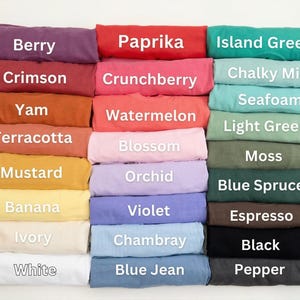May include: A collection of folded t-shirts in various colors, including Berry, Paprika, and Island Green. Each shirt is labeled with its color name in white text. The shirts are neatly stacked, showcasing a range of hues.
