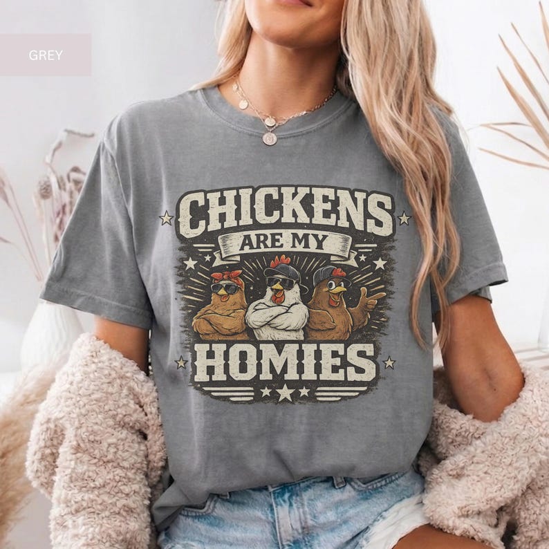 May include: Grey t-shirt with the text "CHICKENS ARE MY HOMIES" and a graphic of three chickens wearing sunglasses and hats. The shirt is a casual, comfortable style.