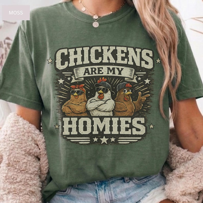 May include: Green t-shirt with the text "CHICKENS ARE MY HOMIES" in a distressed font. The graphic features three cartoon chickens wearing sunglasses and bandanas. The shirt has a crew neck and short sleeves.
