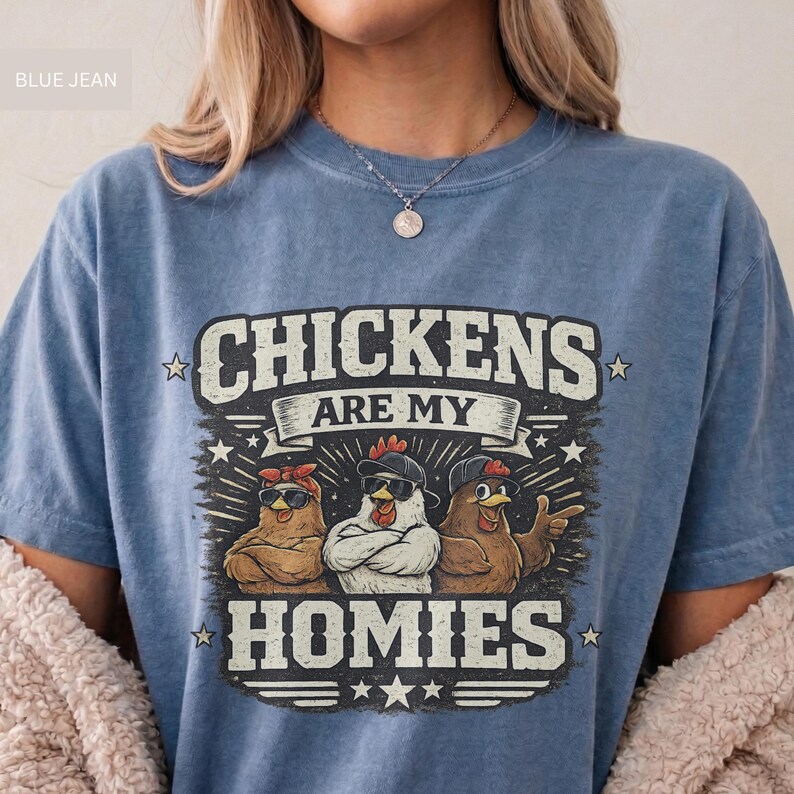 May include: Blue jean-colored t-shirt with the text "CHICKENS ARE MY HOMIES" in a distressed font. The graphic features three chickens wearing sunglasses and bandanas. A fun, casual tee.