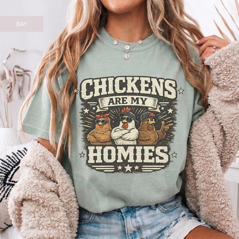 May include: A light green t-shirt with the text "CHICKENS ARE MY HOMIES" in a distressed font. The graphic features three cartoon chickens wearing sunglasses and bandanas. The shirt is a relaxed fit.