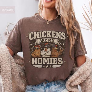 May include: Espresso-colored t-shirt with the text "CHICKENS ARE MY HOMIES" and a graphic of three chickens wearing sunglasses and hats. The shirt has a vintage, worn look.