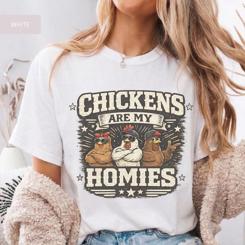 May include: White t-shirt with the text "CHICKENS ARE MY HOMIES" in a distressed, vintage style. The graphic features three cartoon chickens wearing sunglasses and bandanas. The design is surrounded by stars and decorative elements.