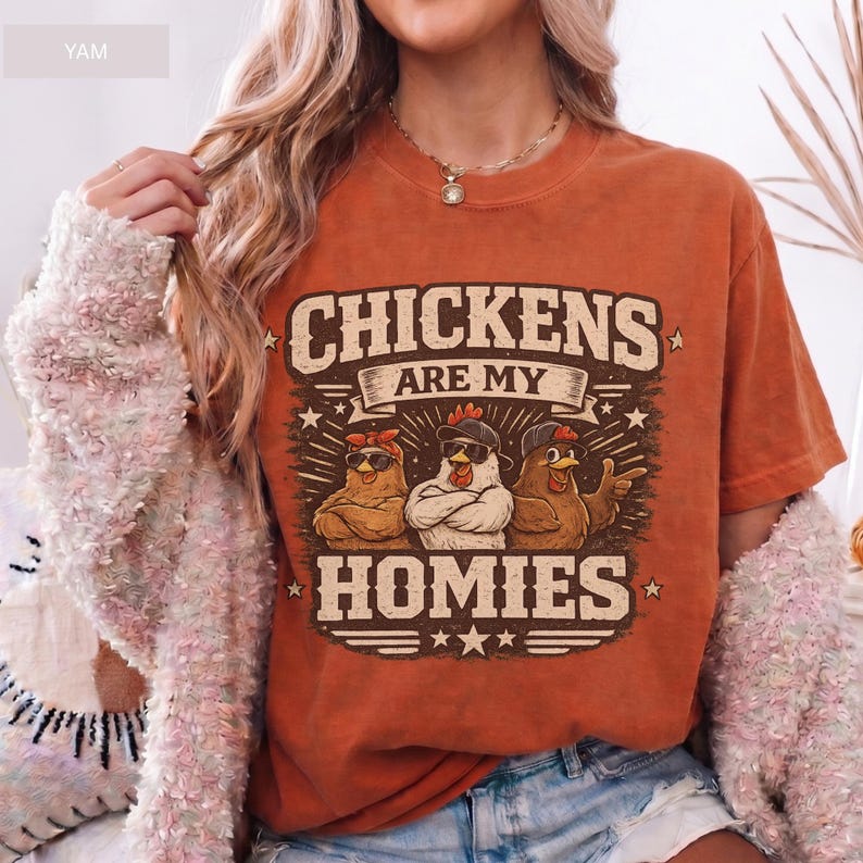 May include: Burnt orange t-shirt with the text "CHICKENS ARE MY HOMIES" in a vintage style. The graphic features three cartoon chickens wearing sunglasses and hats. A fun and quirky design.