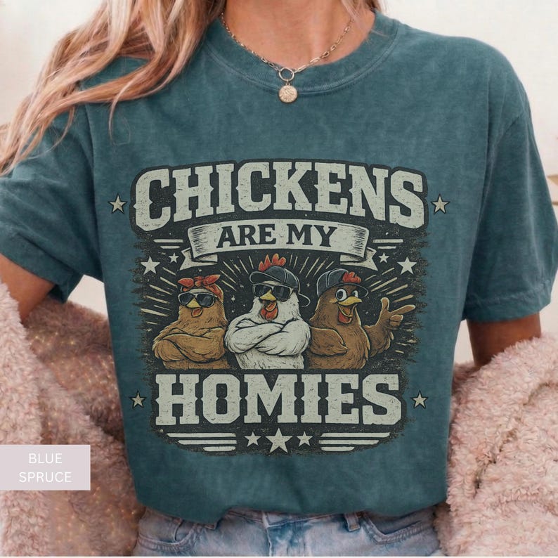 May include: Blue spruce t-shirt with a graphic that reads "CHICKENS ARE MY HOMIES." The graphic features three cartoon chickens wearing sunglasses and hats. The shirt is a comfortable, casual style.