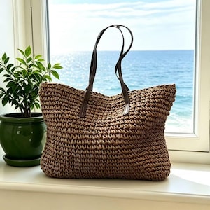 Può includere: Una borsa tote marrone intrecciata con manici in pelle marrone scuro. La borsa è rettangolare con un'ampia apertura e una trama a forma di cestino. I manici sono attaccati con piccoli dettagli in pelle.