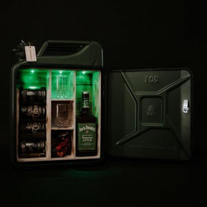 Op de afbeelding: Een olijfgroene metalen jerrycan omgebouwd tot drankkast met een open deur. Het interieur is voorzien van houten planken, groene ledverlichting, een fles Jack Daniel's Tennessee Apple, twee glazen en vier blikjes Royal Crown Cola.