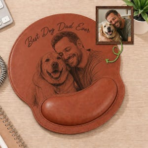 May include: Brown leather mouse pad with a wrist rest, featuring an engraved image of a man and a dog. The text "Best Dog Dad Ever" is above the image. A small framed photo of the same pair is also present.