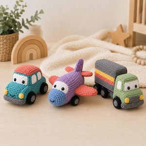 May include: Three handmade crochet toys including a teal car with a coral roof, a purple airplane with coral wings, and a green truck with a gray cargo bed featuring orange and yellow stripes. Each vehicle has white windows and black circular eyes.