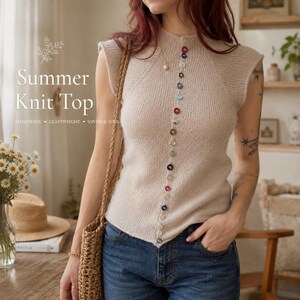 May include: A sleeveless beige knit top featuring a high neckline and a vertical row of multicolored buttons down the center front. The garment is paired with blue denim jeans and a woven straw bag. Text on the image reads Summer Knit Top.