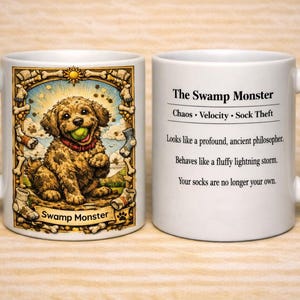 May include: Two white ceramic mugs featuring a brown curly-haired dog holding a green ball. The left mug shows the dog in a bone-patterned frame with the text 'Swamp Monster'. The right mug displays the text 'The Swamp Monster', 'Chaos • Velocity • Sock Theft', and a three-line description about the dog's behaviour.