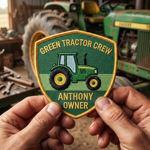 May include: A shield-shaped embroidered patch with a yellow border. The patch features a green tractor graphic, the text GREEN TRACTOR CREW at the top, and the text ANTHONY OWNER at the bottom, all set against a two-tone green background.