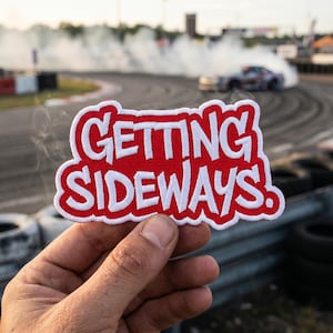 May include: A red and white embroidered patch with the words "GETTING SIDEWAYS!" in a bold, stylized font. The patch is held in front of a blurred background of a race track with a car drifting and producing smoke.