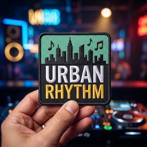 May include: A square embroidered patch with a black border. The top section features a black city skyline silhouette on a light green background with two black musical notes. The bottom section has the white text URBAN and yellow text RHYTHM.