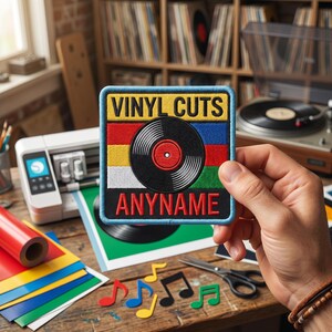 May include: A square embroidered patch with a light blue border, featuring the text VINYL CUTS at the top and ANYNAME at the bottom. The center displays a black vinyl record graphic over horizontal stripes of red, yellow, white, blue, and green.