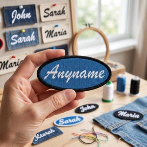 May include: An oval blue patch with the word "Anyname" embroidered in white. The patch is held in a hand, with other name patches and sewing supplies in the background. The patches are made of denim and canvas.