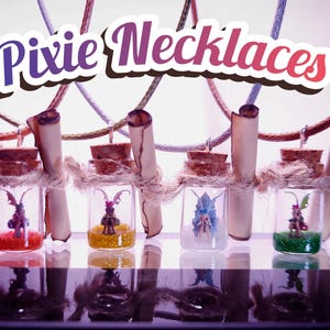 Könnte beinhalten: Feen-Halsketten. Vier kleine Glasflaschen mit Korken, jede enthält eine Miniatur-Feenfigur und eine farbige Basis. Die Flaschen sind an Schnüren aufgehängt, mit gerollten Papierrollen befestigt. Der Text "Pixie Necklaces" steht oben.