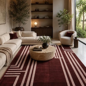 Pode incluir: Um tapete retangular com um fundo bordô profundo e linhas geométricas bege claro que formam um padrão linear estruturado. O tapete está posicionado sobre um piso claro, estendendo-se pelo centro da sala sob uma mesa redonda.