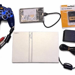 May include: A collection of PlayStation 2 gaming accessories, including a silver console, a blue controller, a hard drive, a memory card, and a power adapter. The controller is dark blue with light blue accents.