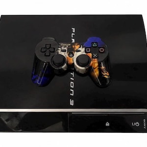 Pode incluir: Uma consola PlayStation 3 preta com acabamento brilhante e o texto PlayStation 3 impresso na parte superior. Um comando de jogo personalizado com uma impressão gráfica de uma personagem está colocado sobre a consola. Os textos 1TB e CUSTOM são visíveis.
