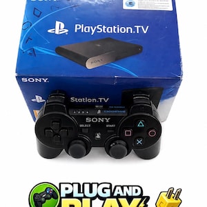 May include: A black PlayStation TV console and controller set. The console is in a blue box with the PlayStation logo and the text "PlayStation.TV". The controller is black with the Sony logo and various buttons. The image also includes the text "PLUG AND PLAY".