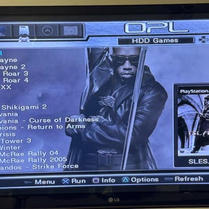 Könnte beinhalten: Ein schwarzer Flachbildfernseher, der ein PlayStation 2-Spielmenü anzeigt. Der Bildschirm zeigt eine Liste von Spielen, darunter "Blade II" und "Castlevania". Ein Werbebild für das Spiel "Blade" ist zu sehen. Der Fernseher hat ein LG-Logo.