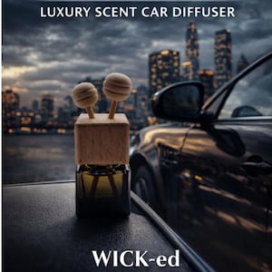 May include: A car air freshener with the text "CREED AVENTUS INSPIRED LUXURY SCENT CAR DIFFUSER" and "WICK-ed GOOD SCENTS VENTURE INTO LUXURY". The diffuser has a wooden top with two spherical accents and sits in a glass bottle.