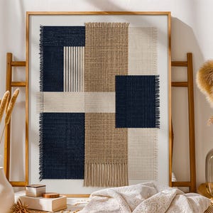 May include: A framed wall art piece featuring a geometric textile collage. The composition includes rectangular panels of navy blue, beige, and cream-colored woven fabric with visible frayed edges and vertical fringe details at the bottom.