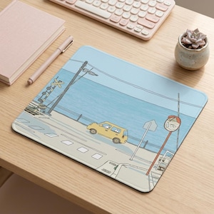 Peut inclure: Un tapis de souris rectangulaire illustrant une route côtière bleu clair avec une voiture jaune, un signal de passage à niveau et un miroir de circulation incurvé. La scène représente un paysage de bord de mer avec un ciel dégagé et une route.