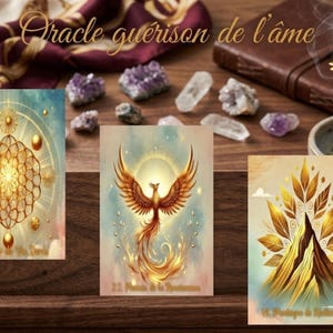 Peut inclure: Trois cartes d'oracle avec des illustrations dorées et aquarelles. Les cartes présentent un mandala doré, un phénix et une montagne avec des feuilles. Les cartes sont sur une surface en bois avec des cristaux et un livre relié en cuir.