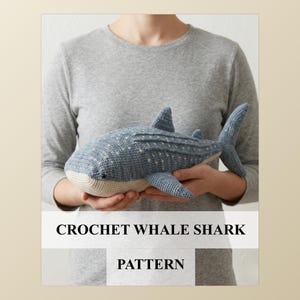 Puede incluir: Un tiburón ballena de ganchillo en tonos azules y blancos. El juguete hecho a mano presenta un diseño detallado con aletas, cola y puntos blancos. El texto "CROCHET WHALE SHARK PATTERN" se muestra debajo. Un objeto suave y tierno.