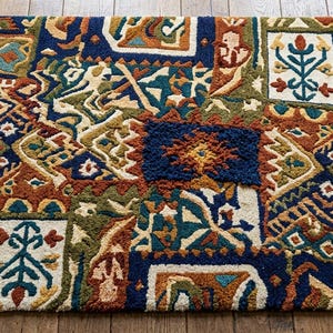 Pode incluir: Um tapete retangular com uma textura densa e tufada com um padrão geométrico e floral multicolorido. O design incorpora tons de azul profundo, laranja ferrugem, verde oliva e creme dispostos num layout complexo de estilo patchwork.