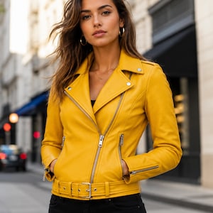 May include: A vibrant mustard yellow motorcycle jacket featuring a notched lapel, silver-toned metal zippers on the front and cuffs, and a matching adjustable belt at the waist with a silver buckle. The jacket has a structured fit and long sleeves.