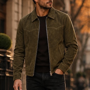 Puede incluir: Una chaqueta de ante verde oliva con cuello clásico, cremallera frontal de metal plateado, mangas largas con puños abotonados y dos bolsillos laterales. La chaqueta se lleva sobre un suéter marrón oscuro y unos vaqueros oscuros.