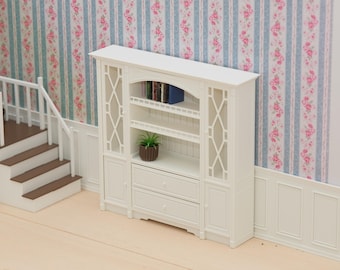 Puede incluir: Una alacena blanca en miniatura para casa de muñecas con dos armarios laterales acristalados con diseño de rombos, dos cajones inferiores con pomos redondos y estantes centrales abiertos. Contiene una pequeña planta verde y libros en miniatura.