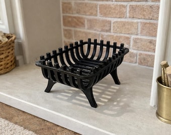 Puede incluir: Una rejilla de chimenea de metal negro con marco rectangular y barras verticales, sostenida por cuatro patas curvas. La rejilla presenta una base de listones y un diseño superior abierto, construido a partir de varillas de metal interconectadas.