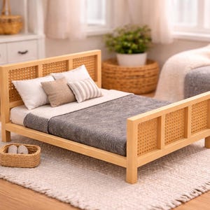 Könnte beinhalten: Ein Miniatur-Holzbett mit einem gewebten Kopf- und Fußteil. Das Bett ist mit weißer und grauer Bettwäsche und mehreren Kissen ausgestattet. Ein kleiner gewebter Korb mit Schuhen steht am Fußende des Bettes. Das Bett steht auf einem hellfarbigen Teppich.