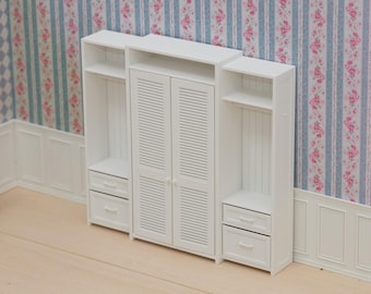Puede incluir: Un armario de casa de muñecas de madera blanca que presenta un gabinete central con puertas de persiana, flanqueado por dos secciones de estantes abiertos. Cada sección lateral incluye dos cajones pequeños en la parte inferior con pomos blancos.