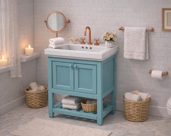 Puede incluir: Un mueble de baño azul claro con lavabo blanco, grifo y herrajes de cobre. El mueble tiene dos puertas y un estante inferior abierto con toallas blancas dobladas y una pequeña cesta tejida. Un espejo redondo de cobre se sitúa encima.
