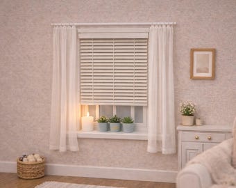 Puede incluir: Una escena de ventana en miniatura con persianas horizontales blancas enmarcadas por cortinas blancas transparentes en una barra. En el alféizar hay una vela de pilar blanca y tres pequeñas plantas verdes en macetas.