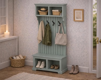 Puede incluir: Un mueble recibidor de madera color verde salvia que incluye un banco con dos compartimentos de almacenamiento inferiores, un panel vertical con cuatro ganchos de metal negro y un estante superior con dos cestas tejidas y una tela doblada.