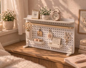 Puede incluir: Un organizador de escritorio tipo tablero perforado en color blanco con una repisa superior, una barra de madera y varios accesorios, incluyendo dos bandejas pequeñas, un recipiente para flores secas, un calendario, un reloj y unas tijeras.