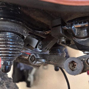 May include: Close-up of a bicycle's suspension system, showcasing black components, including a shock absorber, linkages, and bolts. The image highlights the mechanical details of the bike's frame and suspension.