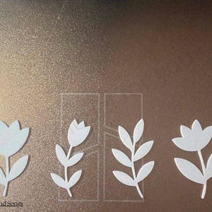 May include: Four white die-cut floral and leaf shapes arranged in a row on a metallic bronze surface. The designs include two tulip-like flowers and two leafy stems. The text "@Games and Songs" is printed in the bottom left corner of the image.