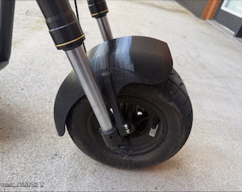 May include: A black electric scooter front wheel assembly featuring a thick, textured black plastic mudguard, a black rim with a pneumatic tire, and a silver metal telescopic suspension fork with black housing and thin gold accent rings.
