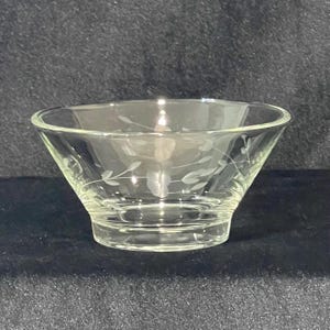 May include: Clear glass bowl with a flared shape and etched floral design. The bowl has a wide opening and a sturdy base. The etched design features delicate leaves and stems, adding a touch of elegance to the glassware.