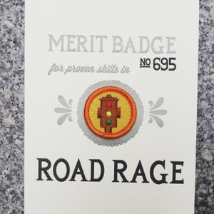 May include: A merit badge for road rage. The badge is round and features a traffic light with red, yellow, and green lights. The badge is orange and yellow with a white background. The text on the badge reads "Merit Badge No. 695 for proven skills in Road Rage".