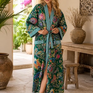 May include: A floor-length green robe featuring a vibrant, multi-coloured floral and paisley print. The garment includes long sleeves with white and green striped cuffs, a matching striped shawl collar, and a tie belt at the waist with pockets.